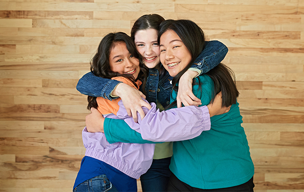 three teen girls in a group hug, posing and smiling for the camera